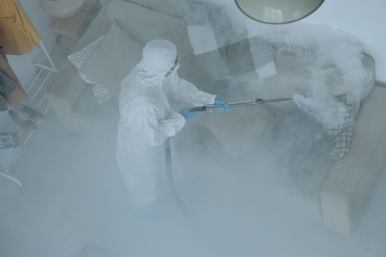 Woman in PPE cleaning a sofa with a chemical spray